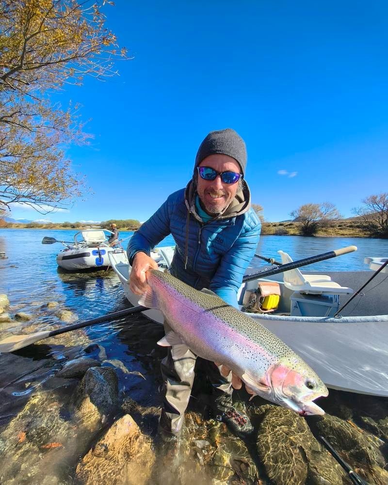 A guide smiling with a rainbow trout beside a drift boat