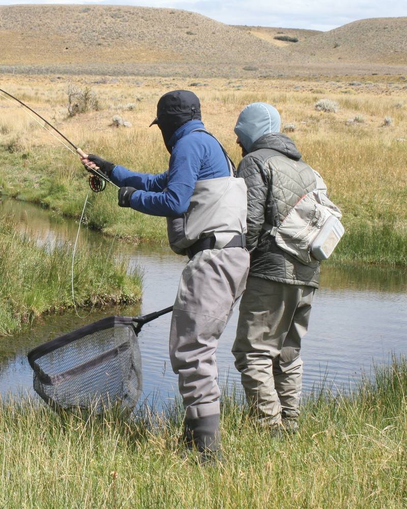 A guide helps an angler net a trout on a small Patagonian stream