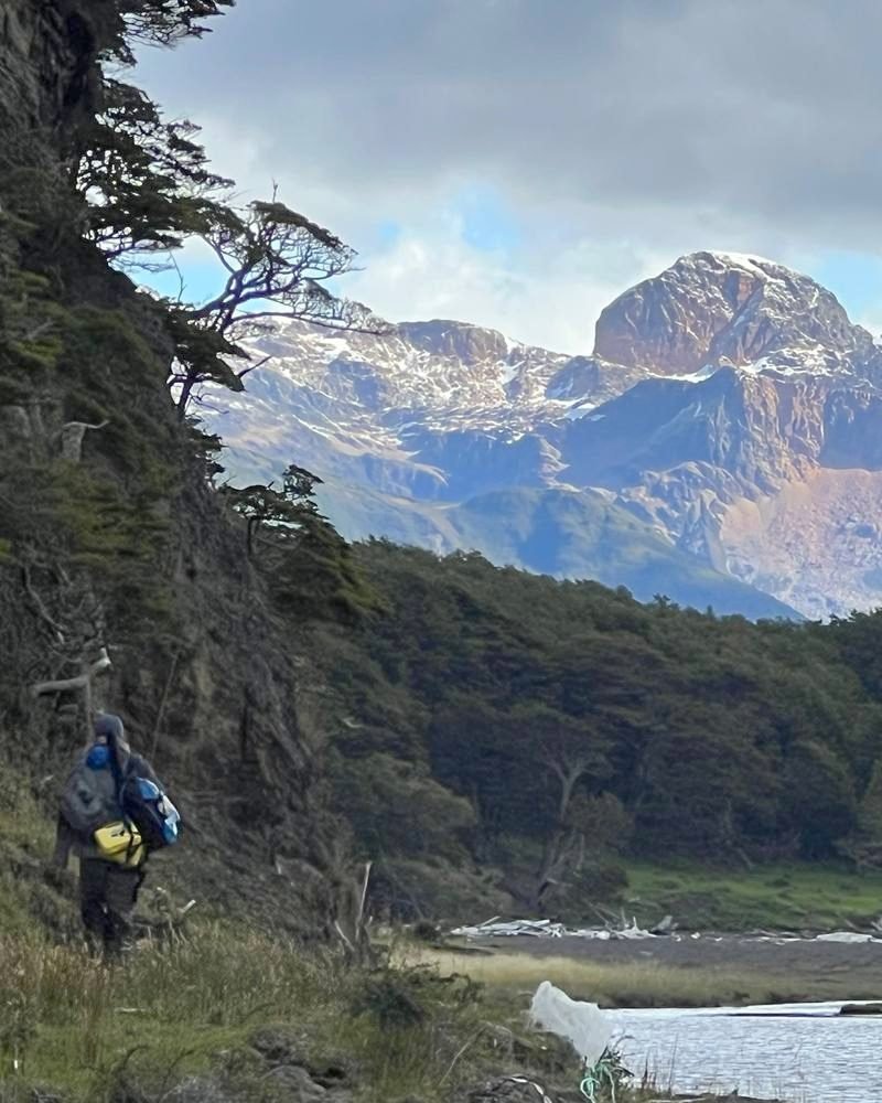 An angler walks toward remote water with a snow-capped Patagonian peak ahead